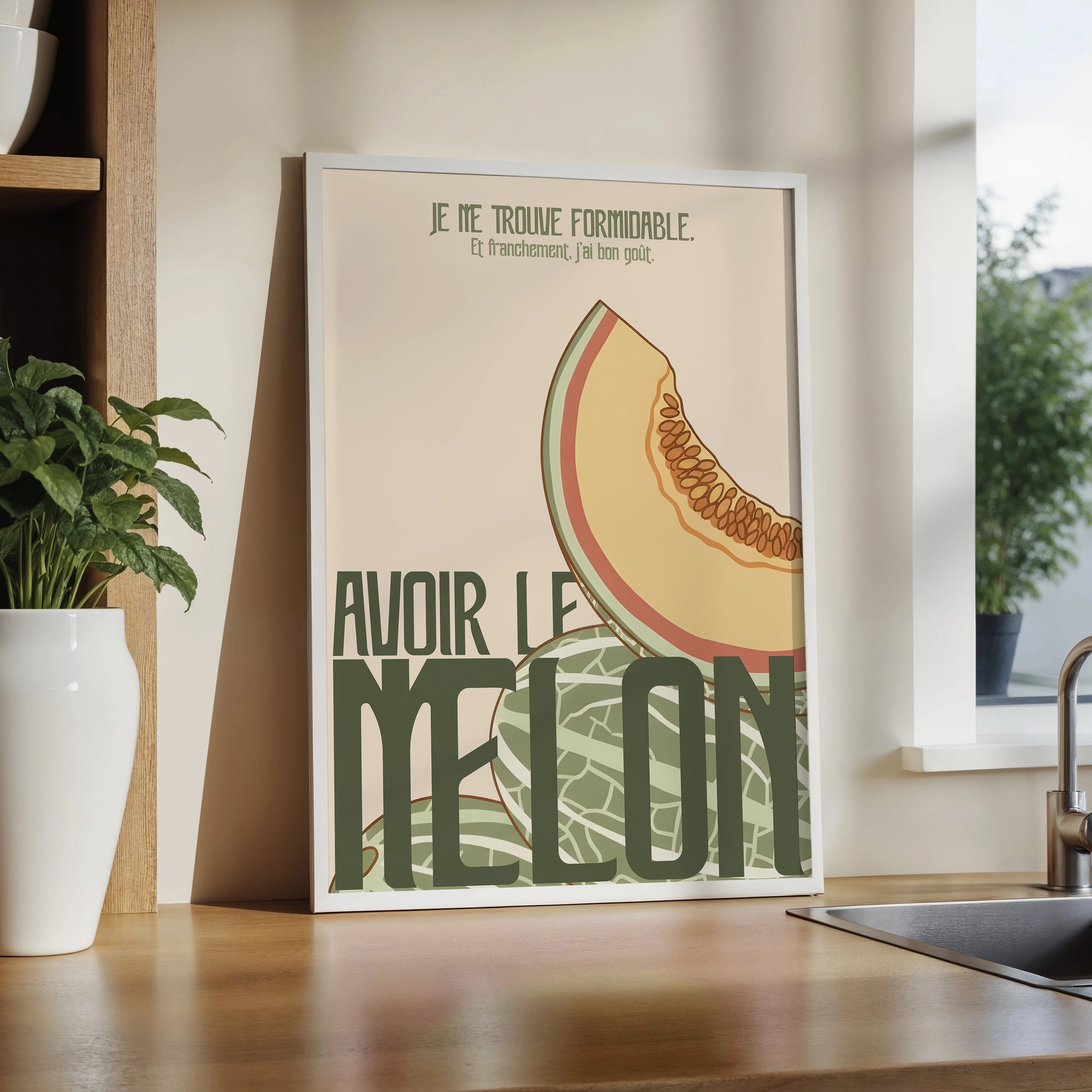 Poster « Avoir le melon » posé sur un plan de travail de cuisine en bois. Illustration rétro pastel avec tranche de melon, peau en motif vert, texte humoristique en lettres vert foncé. Cadre blanc fin. Décor lumineux avec plante verte, bocaux et éléments de cuisine, ambiance naturelle et moderne orientée déco murale.