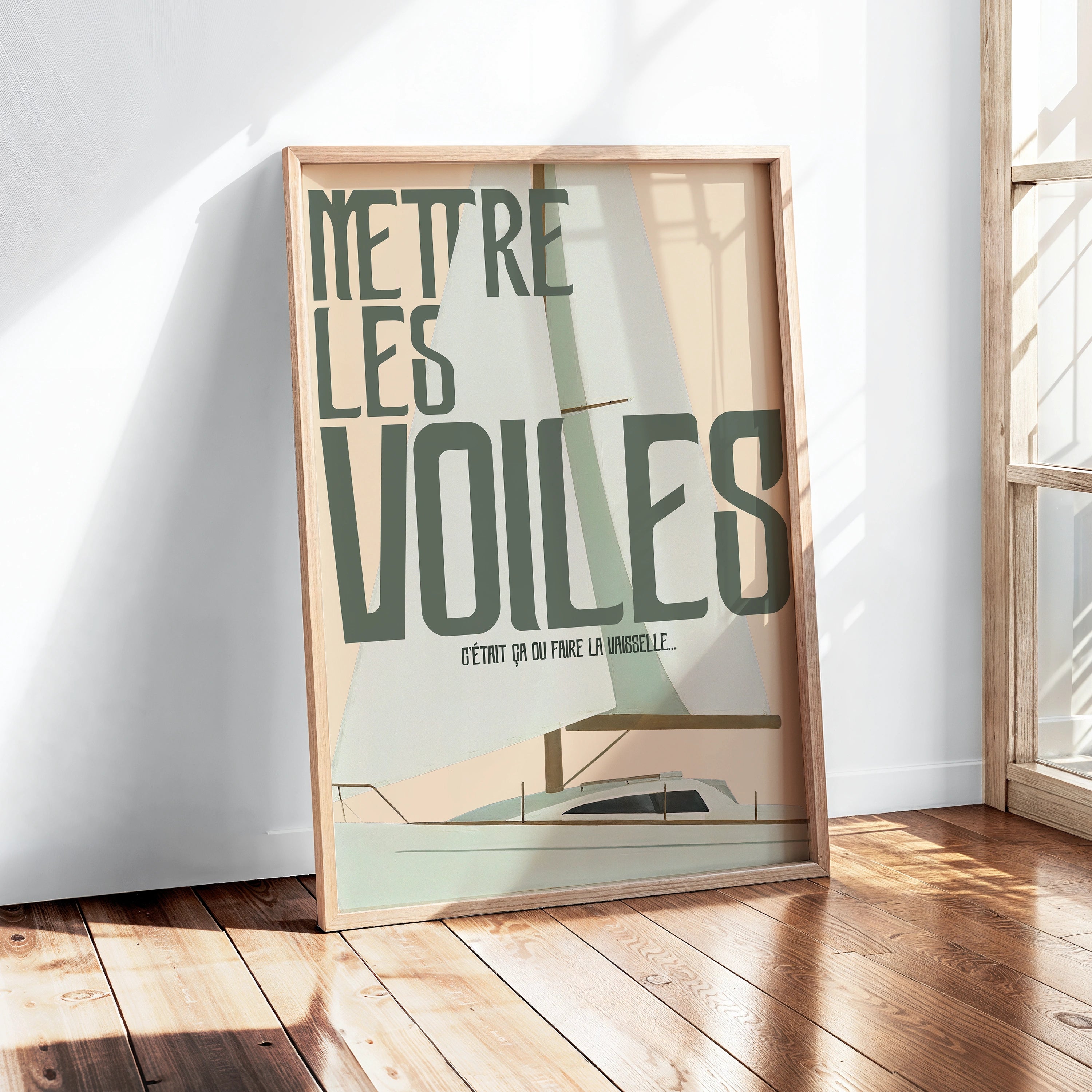 Affiche “Mettre les voiles” en grand cadre bois posé au sol, éclairage naturel fort. Illustration d’un bateau à voile stylisé, palette pastel vert sauge et sable, typographie large et déstructurée. Décor lumineux type intérieur moderne avec plancher en bois clair.