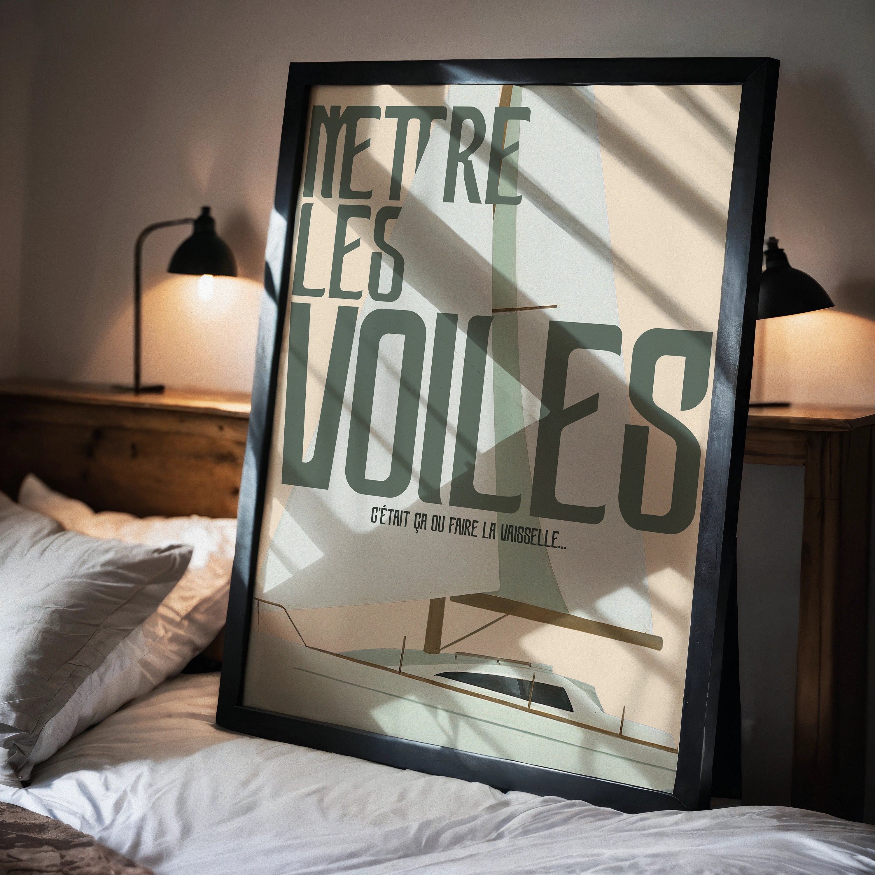 Affiche “Mettre les voiles” en cadre noir, posée sur un lit dans une chambre chaleureuse. Illustration flat d’un voilier, grandes voiles vert d’eau et sable, typographie rétro allongée. Ombres marquées du matin, lampe de chevet noire, ambiance intime et contemporaine.
